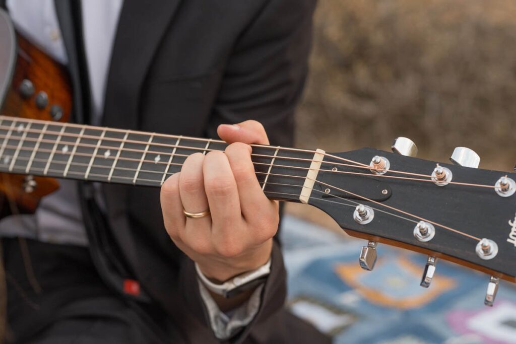 Groom's hand is playing guitar with wedding band on.