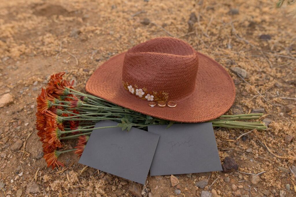 Red hat with bouquet of red carnations and love letters sitting on the ground in the desert.