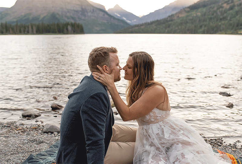 Bride and Groom kiss while sitting on rocky shoreline at Glacier National Park Elopement.