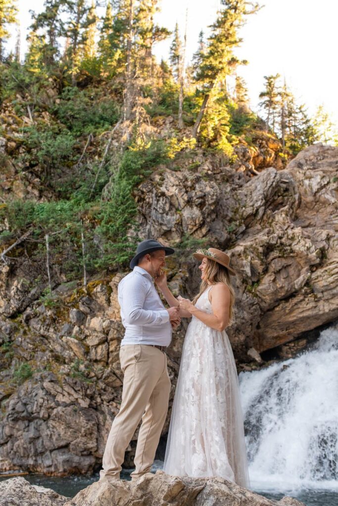 Couple smiling while standing on rock in front of Running Eagle Falls for Glacier National Park Elopement.