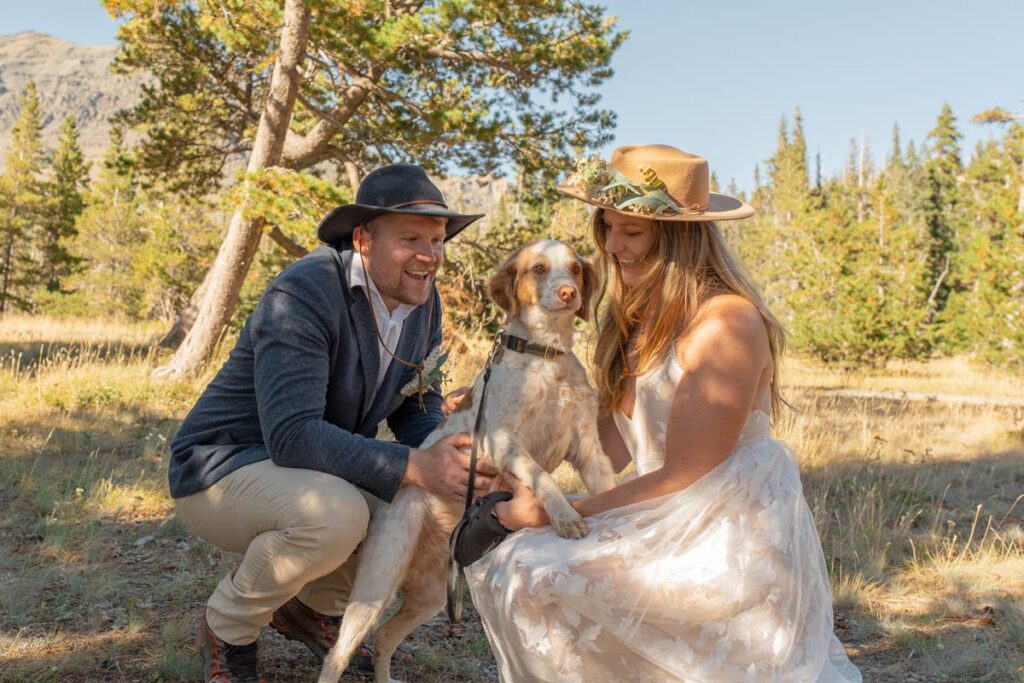 Bride and groom crouch down pet their dog during Glacier National Park Elopement.