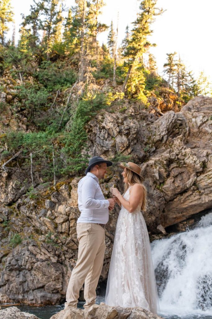 Bride and groom laugh together in front of Running Eagle Falls at Glacier National Park.