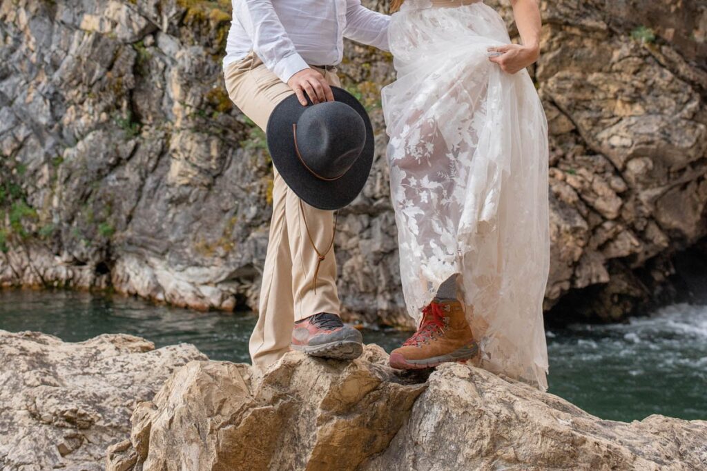 Bride and groom's hiking boots as they step up on a rock next to a waterfall.