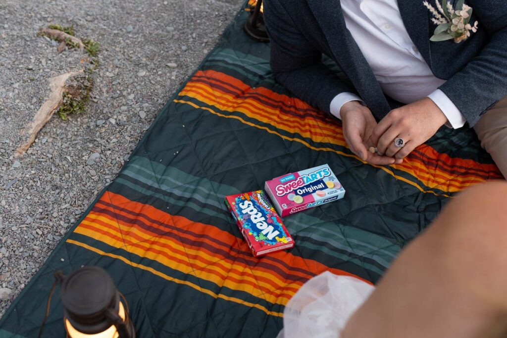 Bride and groom share candy together on a blanket.