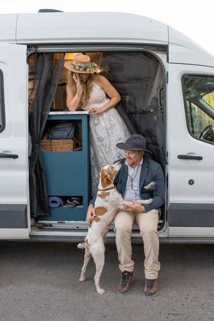 Bride and groom hang out in white camper van with their dog.