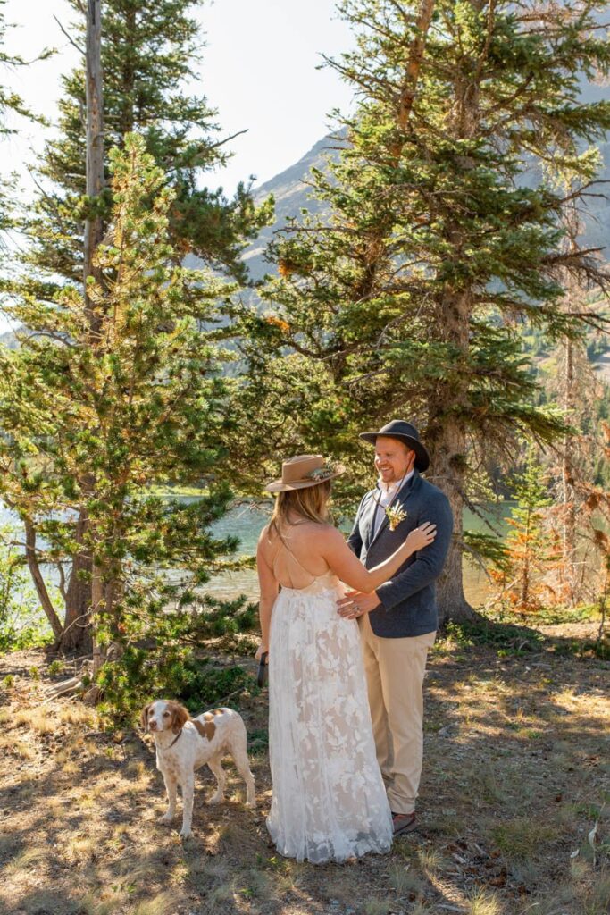 Couple share a first look with their dog in front of pine trees in the mountains.