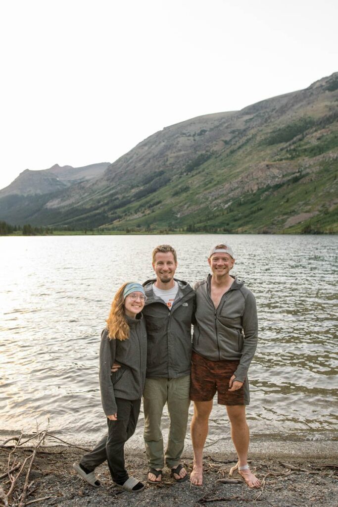Three friends stand on shore of Poia Lake in Glacier National Park after the sun has set.