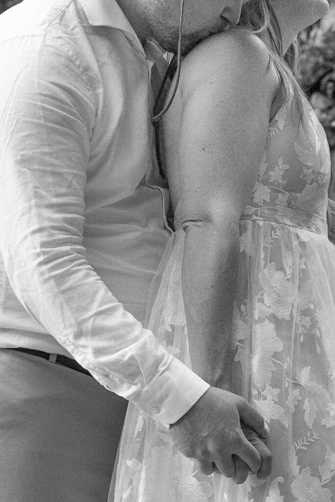 Black and white image of groom kissing bride's shoulder.