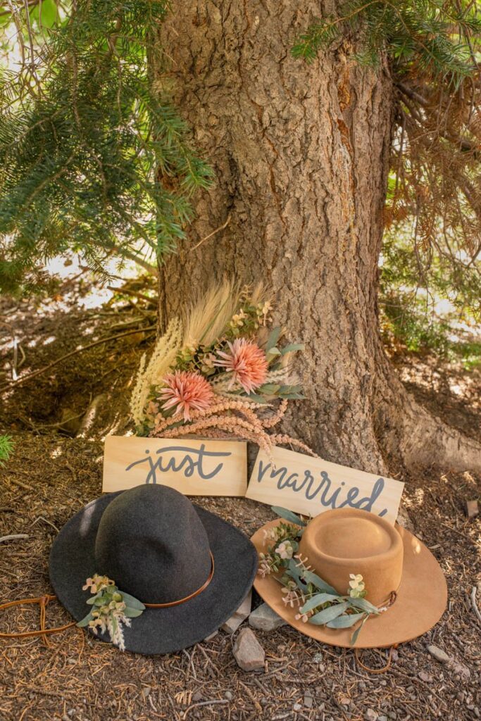 Hats, flowers, and signs sitting under tree for Glacier National Park Elopement.