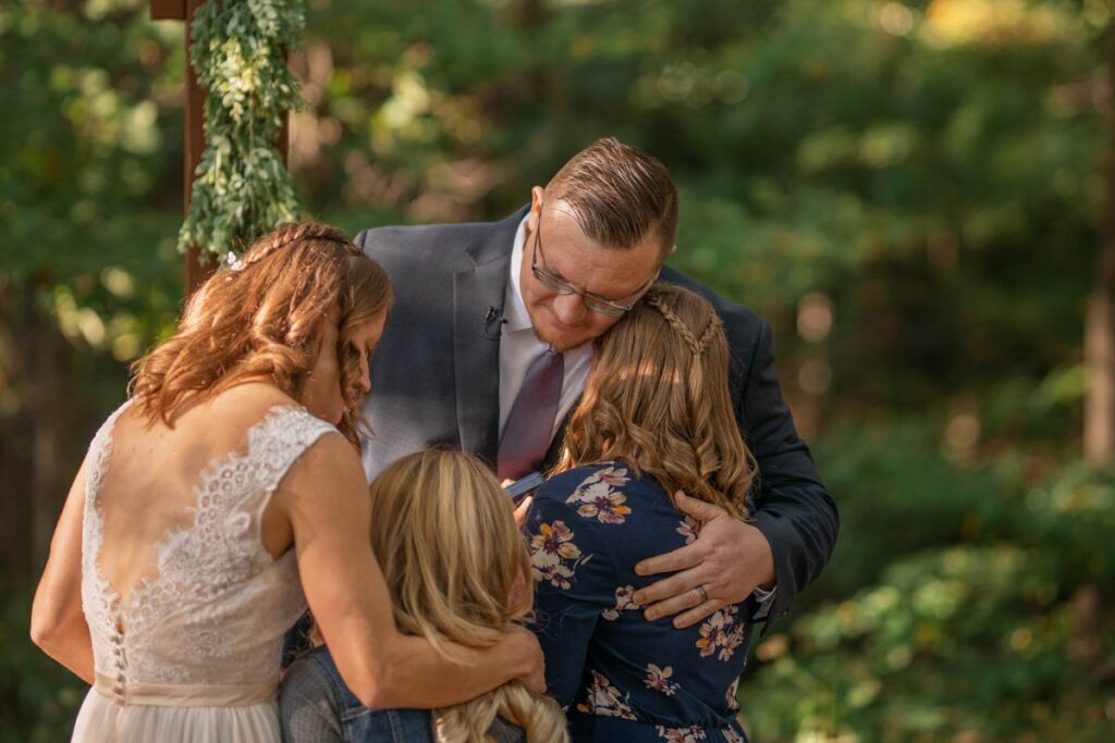 Bride and groom hug daughters during elopement ceremony.