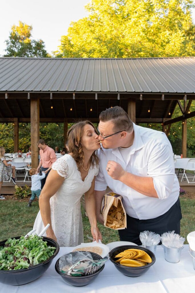 Bride and groom kiss as they grab food at the taco bar during the reception.