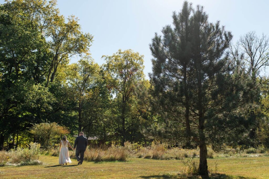 Bride and groom walk through a meadow on  their sunny, fall elopement day.