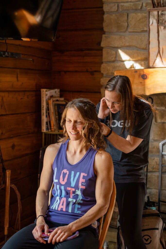 Bride's friend doing her hair as they get ready in log cabin.