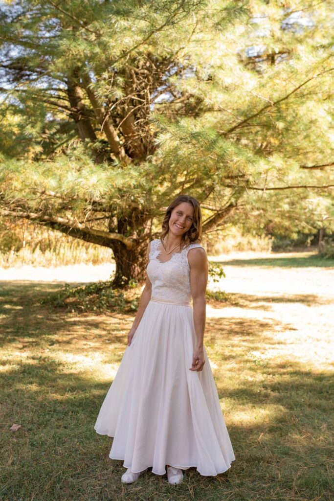 Bride smiles while standing under an evergreen tree.