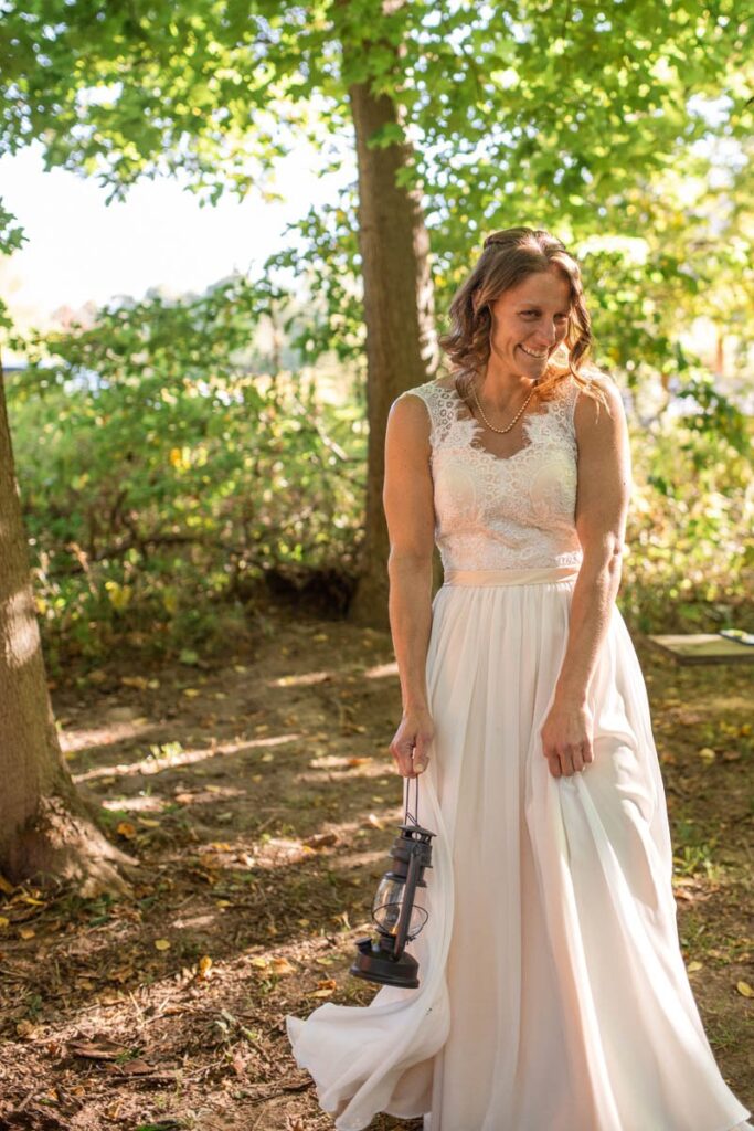 Bride happily walks down aisle for wooded wedding ceremony carrying a lantern.