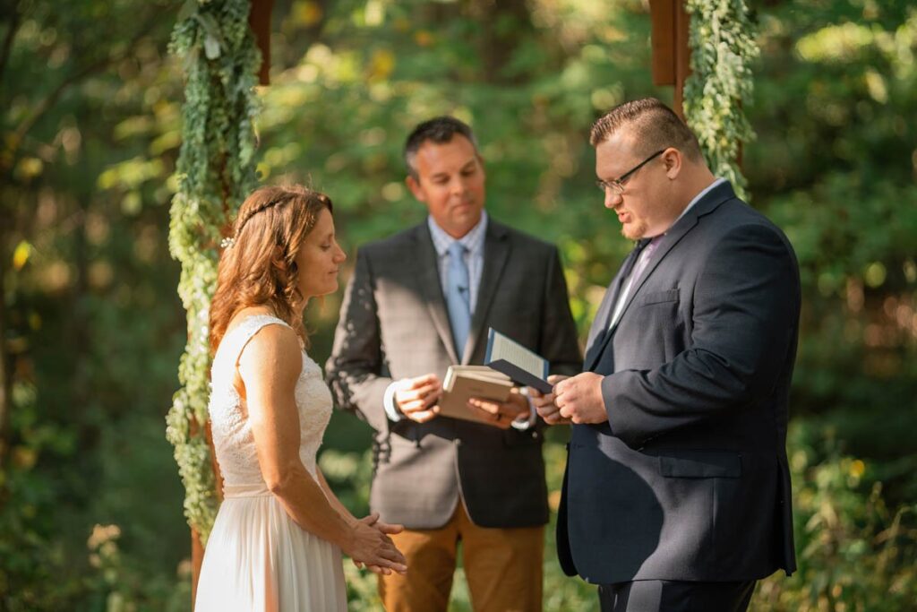 Groom reading his vows to the bride by an arch with officiant.