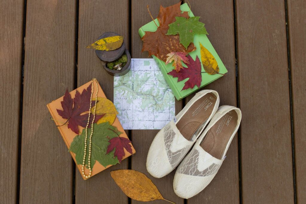 Flatlay of details including shoes, map, books, leaves, wedding rings, and pearl necklace.