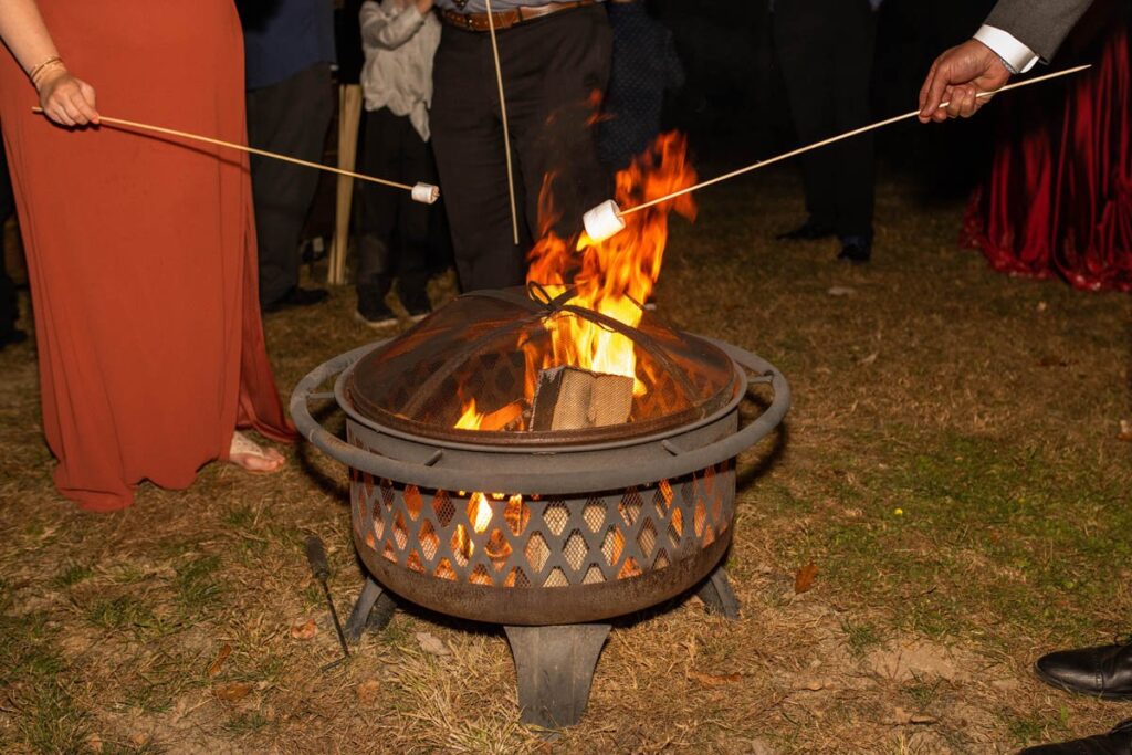 Wedding guests roast marshmallows over a bonfire during reception.