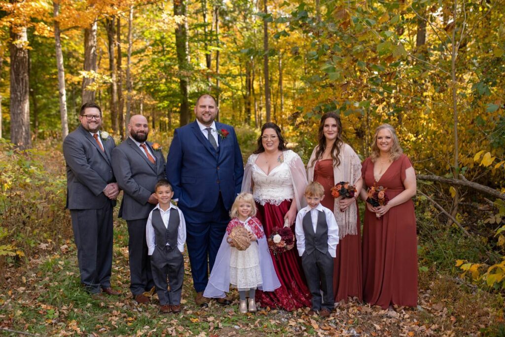 Wedding party stands with bride, groom, flower girl, and two ring bearers in the woods.