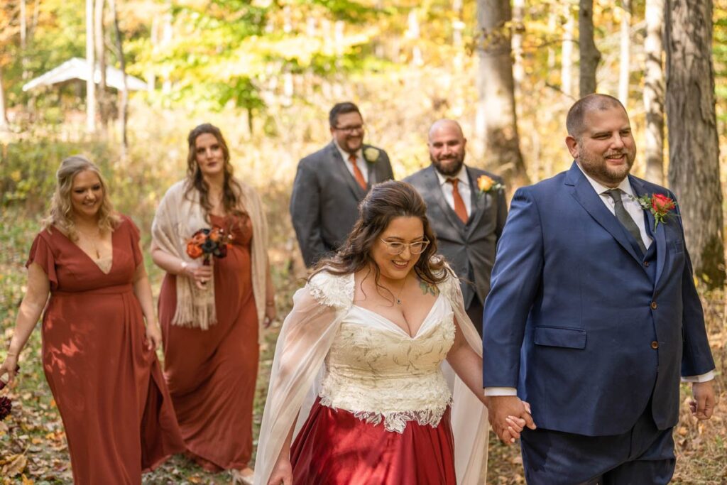 Bridal party walks together on a trail in the woods.