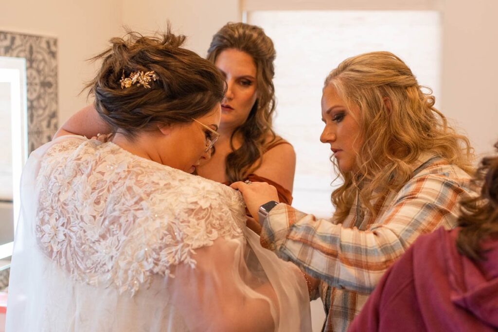 Bridesmaids helping bride to get into her dress at her wedding at Owl Ridge.