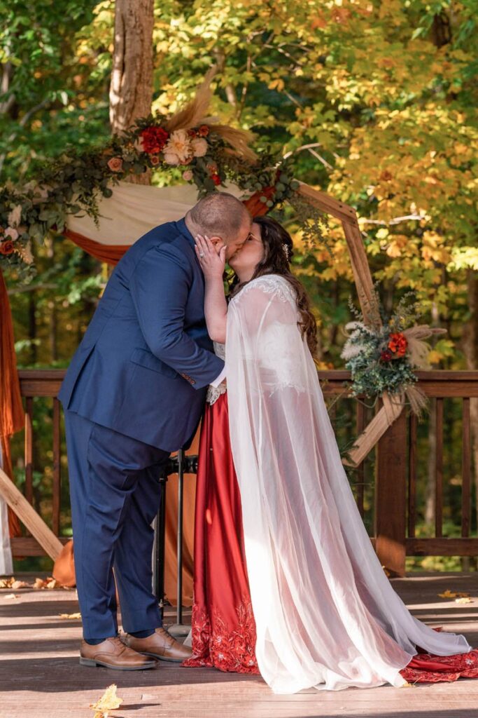 First kiss between bride and groom at Owl Ridge wedding in the fall.