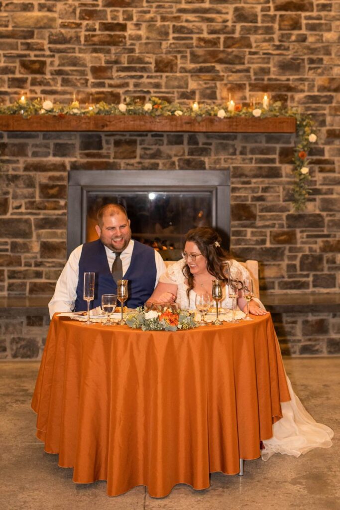Bride and groom laugh as they sit at their sweethearts table during wedding reception at Owl Ridge.