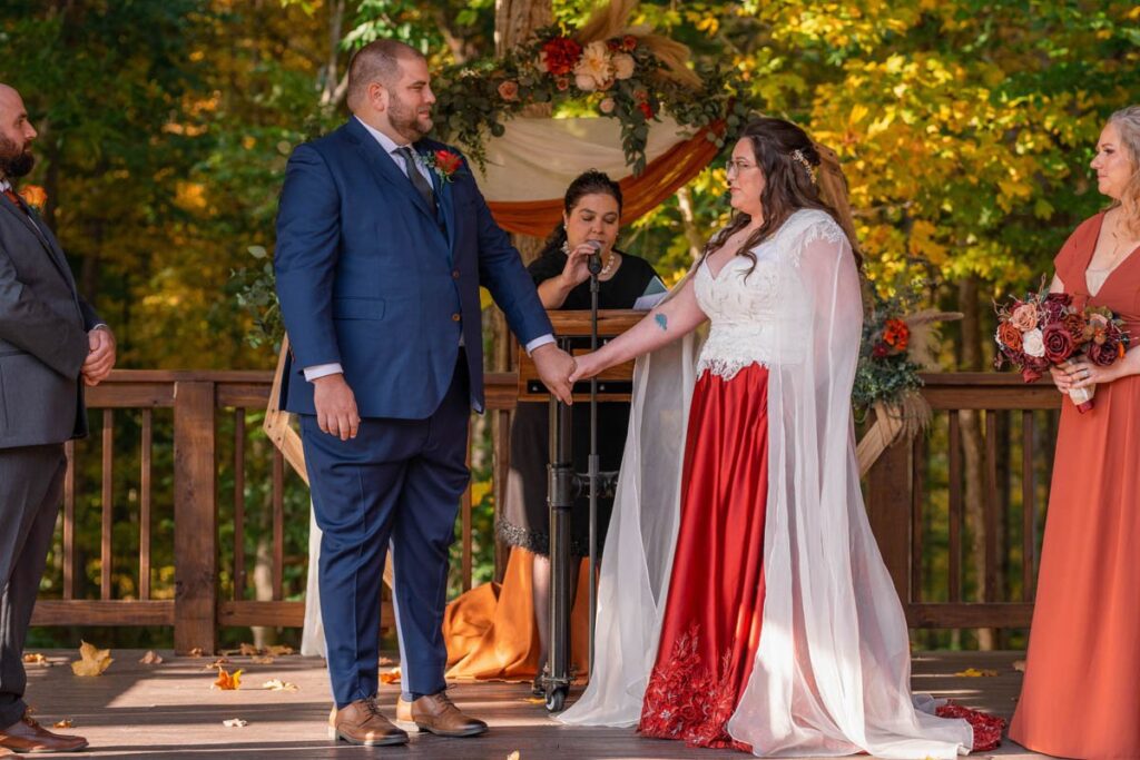Bride and groom hold hands and look at one another teary-eyed during wedding ceremony.