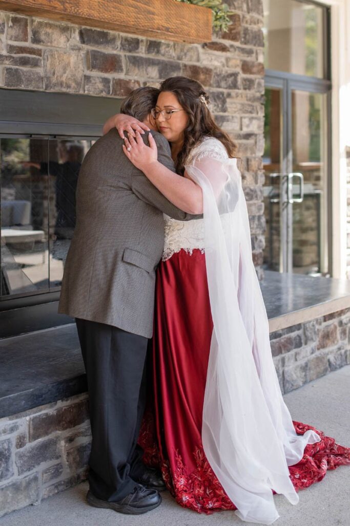 Bride hugs grandfather on her wedding day in front of outdoor fireplace.