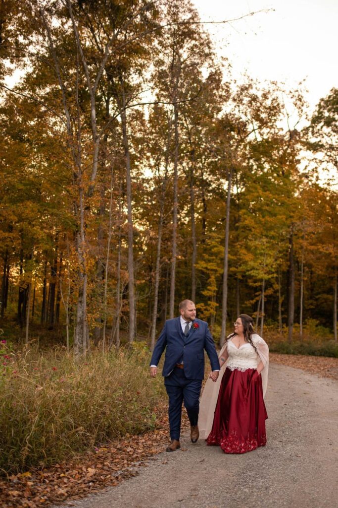 Groom and bride hold hands while walking at sunset at Owl Ridge Wedding Venue.