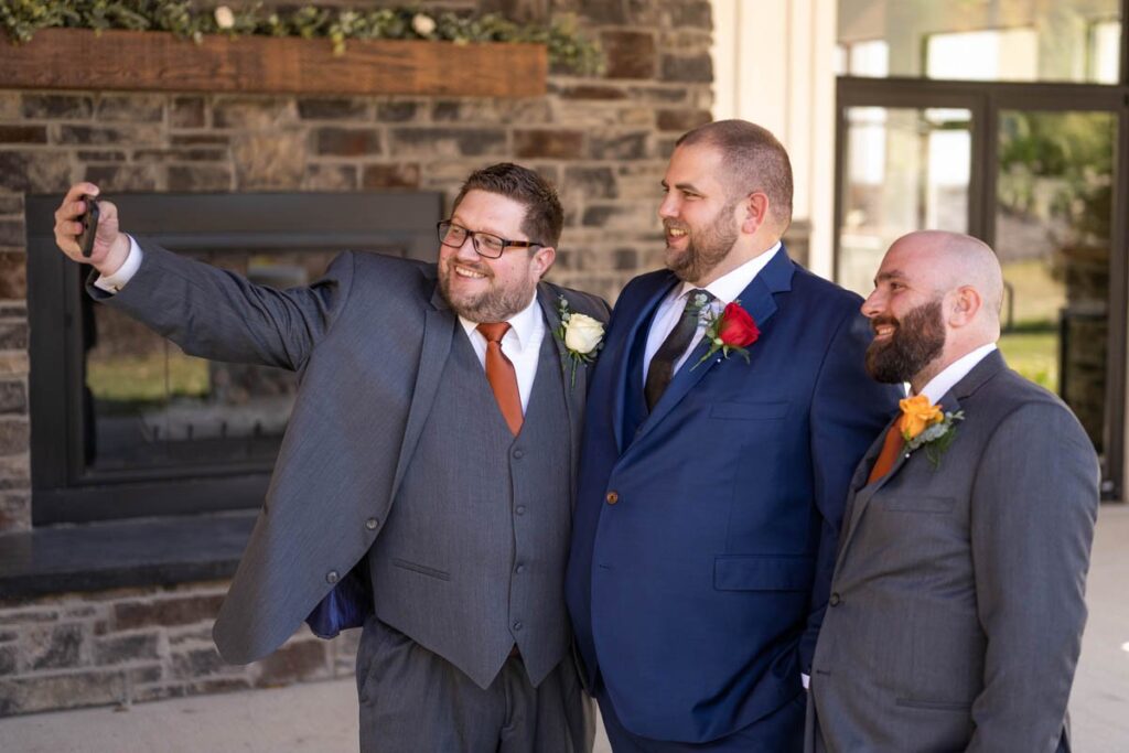 Groom and groomsmen gather together for a selfie after getting into suits.