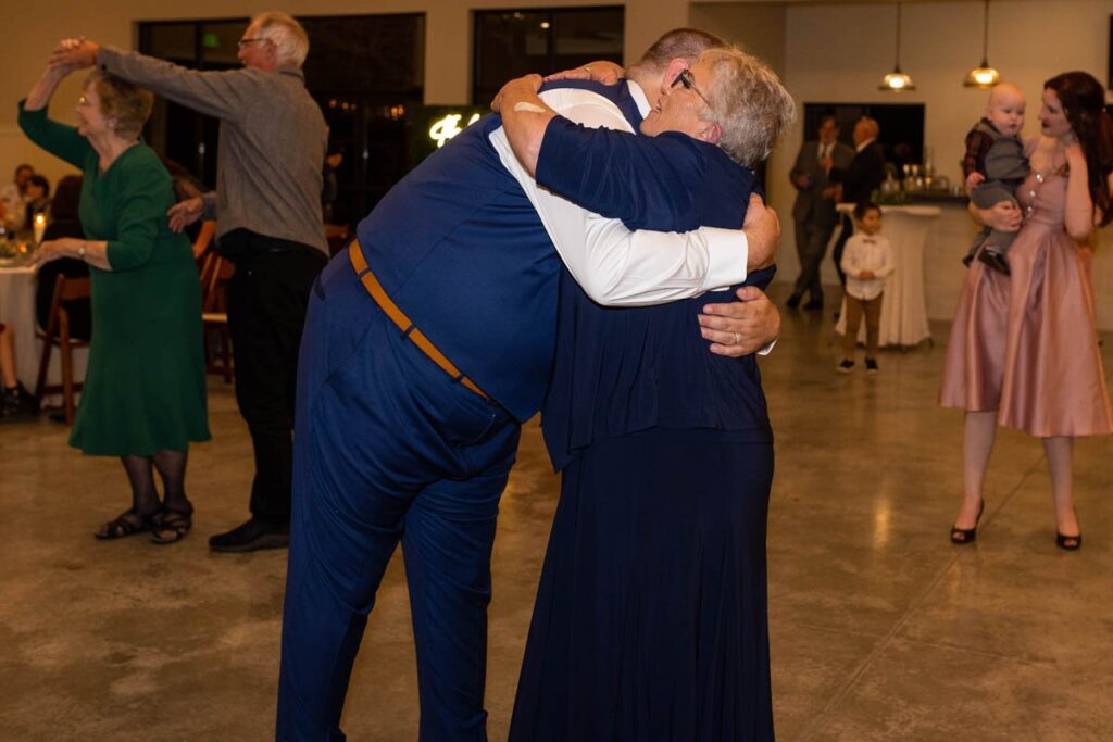Groom hugs mother after mother and son dance at wedding reception.