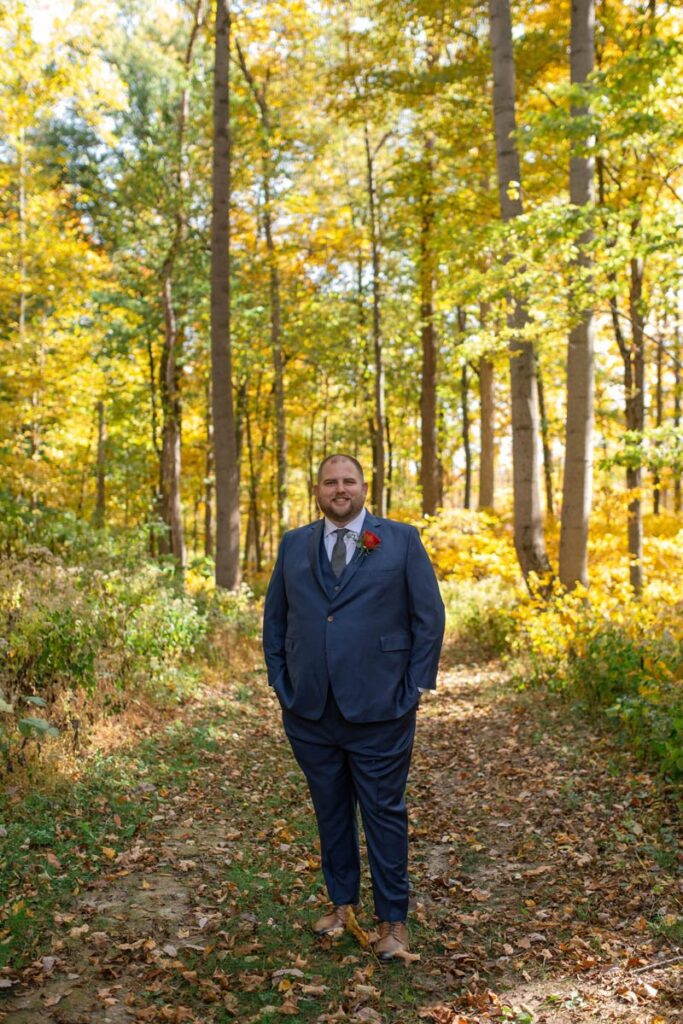 Groom stands smiling in the woods.