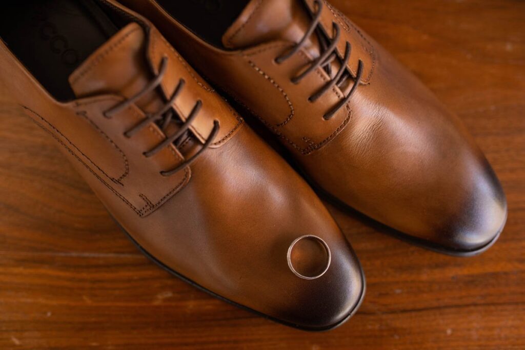 Groom's wedding band rests on his brown leather shoes.