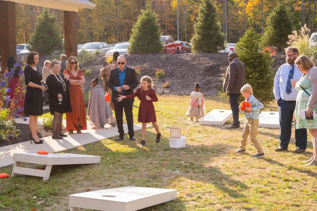Wedding guests play cornhole outside at fall wedding.