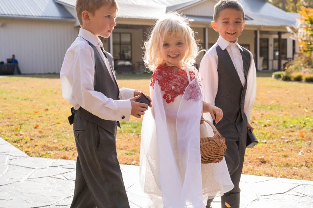 Smiling flower girl and ring bearers walk down aisle.