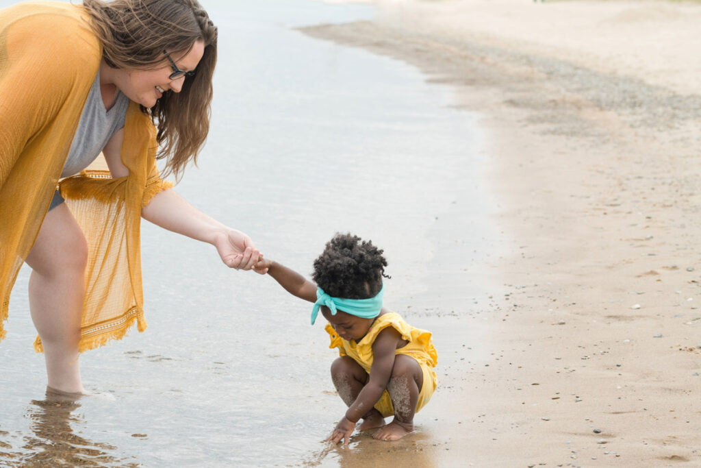 Mother holds daughter's hand while she plays on the shore.