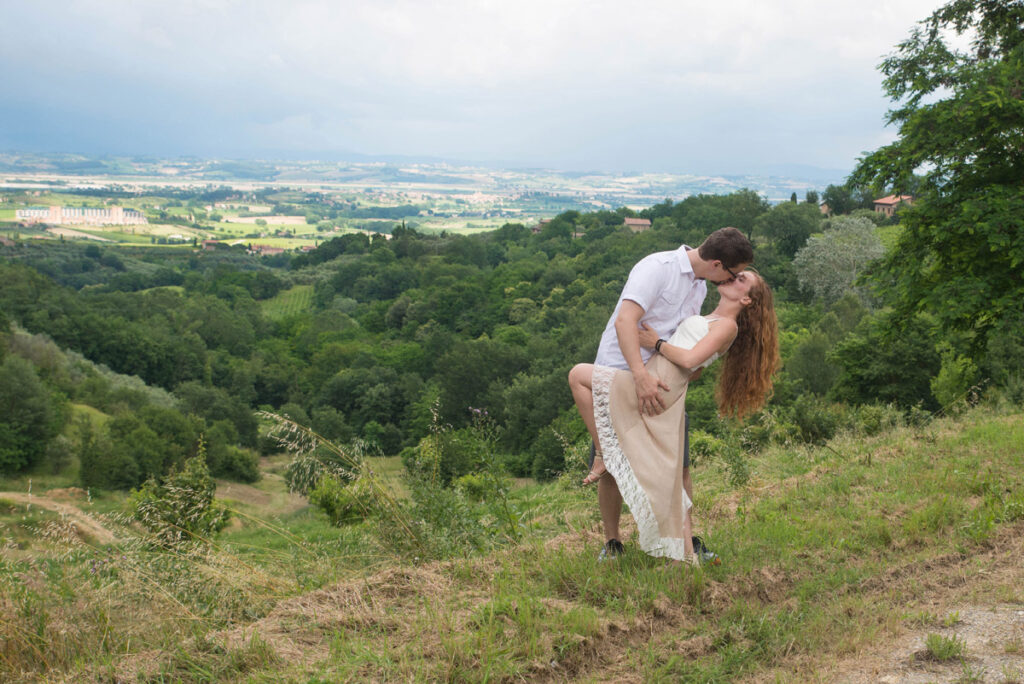 Man dips woman for a kiss with Tuscany behind them.