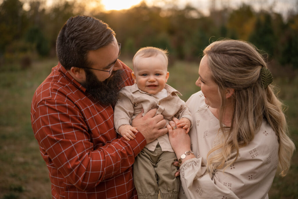 Parents hold their son up and look at him while he smiles.