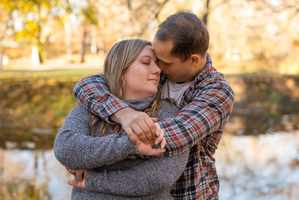 Couple snuggles in closely with eyes closed near a creek.