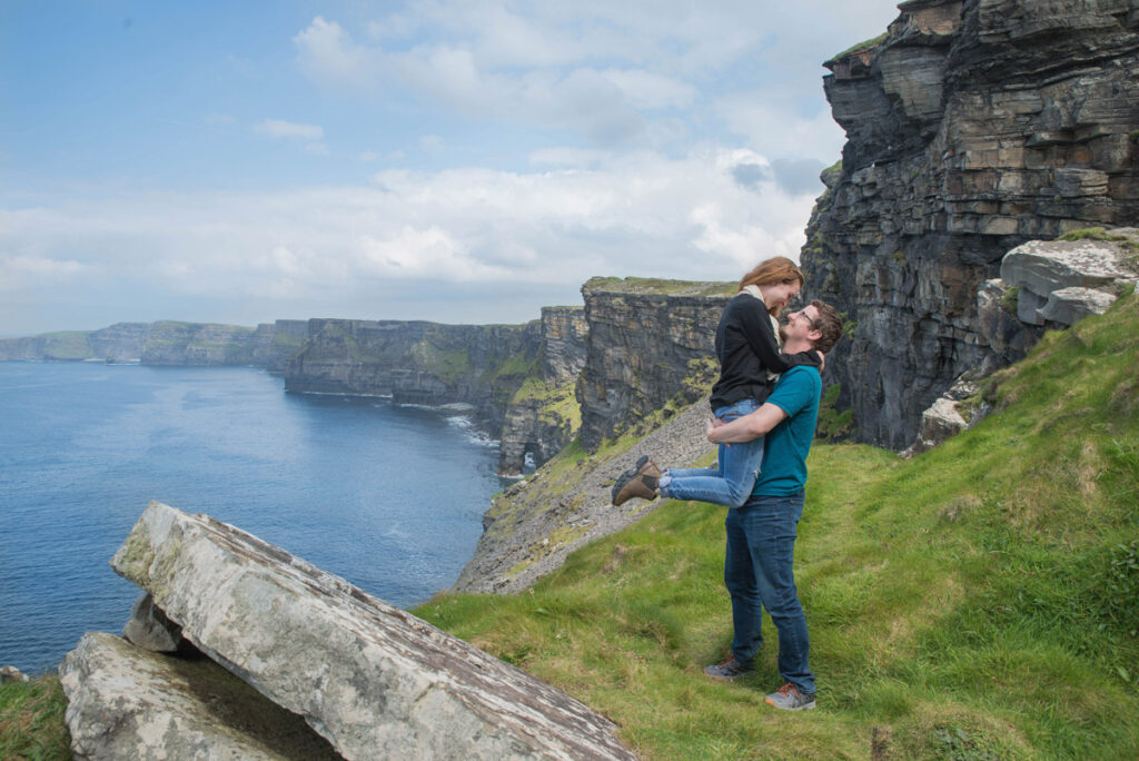 Man lifts woman while they stand on Cliffs of Moher.