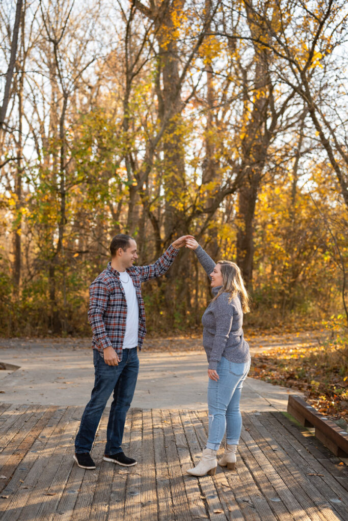 Couple dances on a wooden bridge during fall photo session.