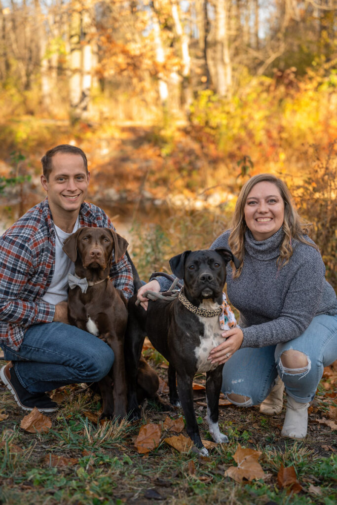 Couple smiles while crouching next to their two dogs.