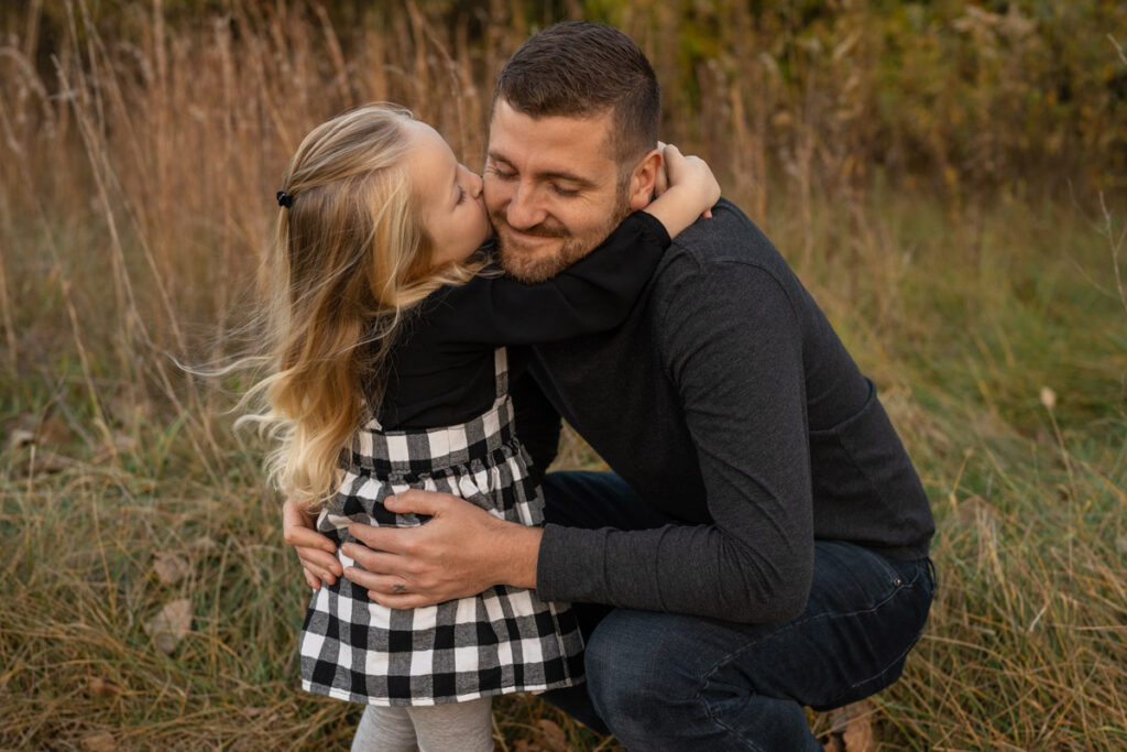 Daughter hugs father and gives him a kiss on the cheek.