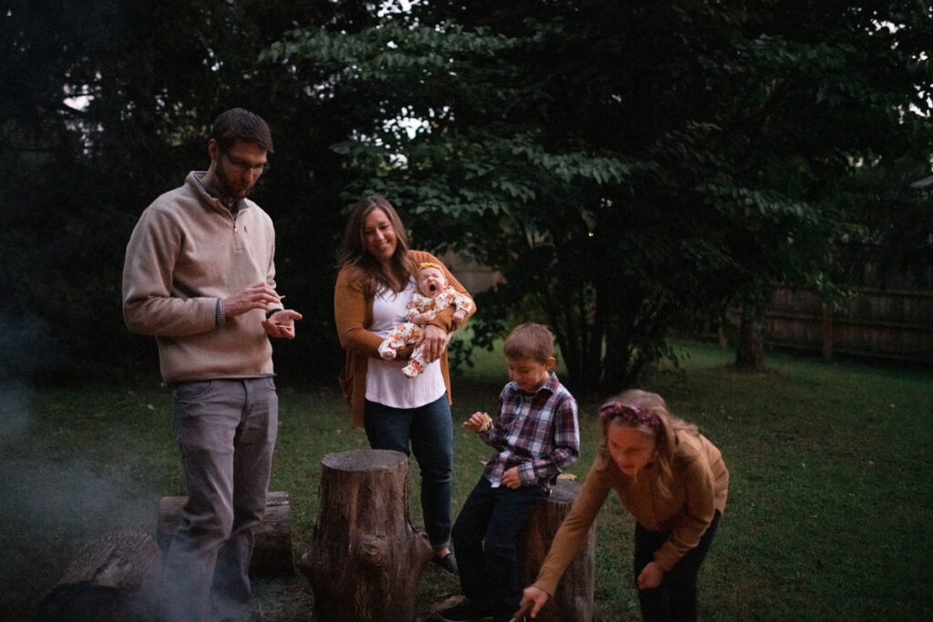 Couple stands around bonfire at night and baby yawns.