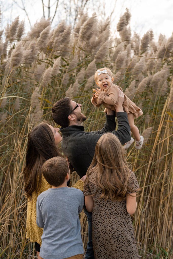 Family holds up daughter while she laughs and claps her hands.