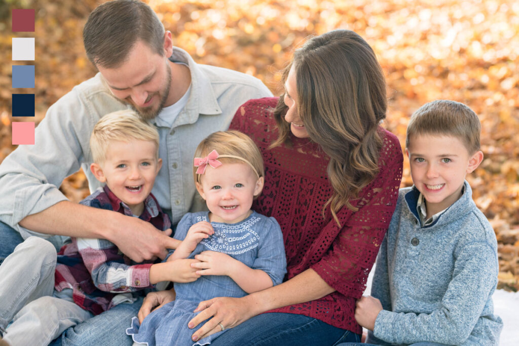 Family laughs together while sitting among gold fallen leaves.