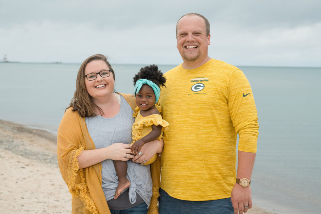 Family of 3 dressed in yellow smiling on the beach.