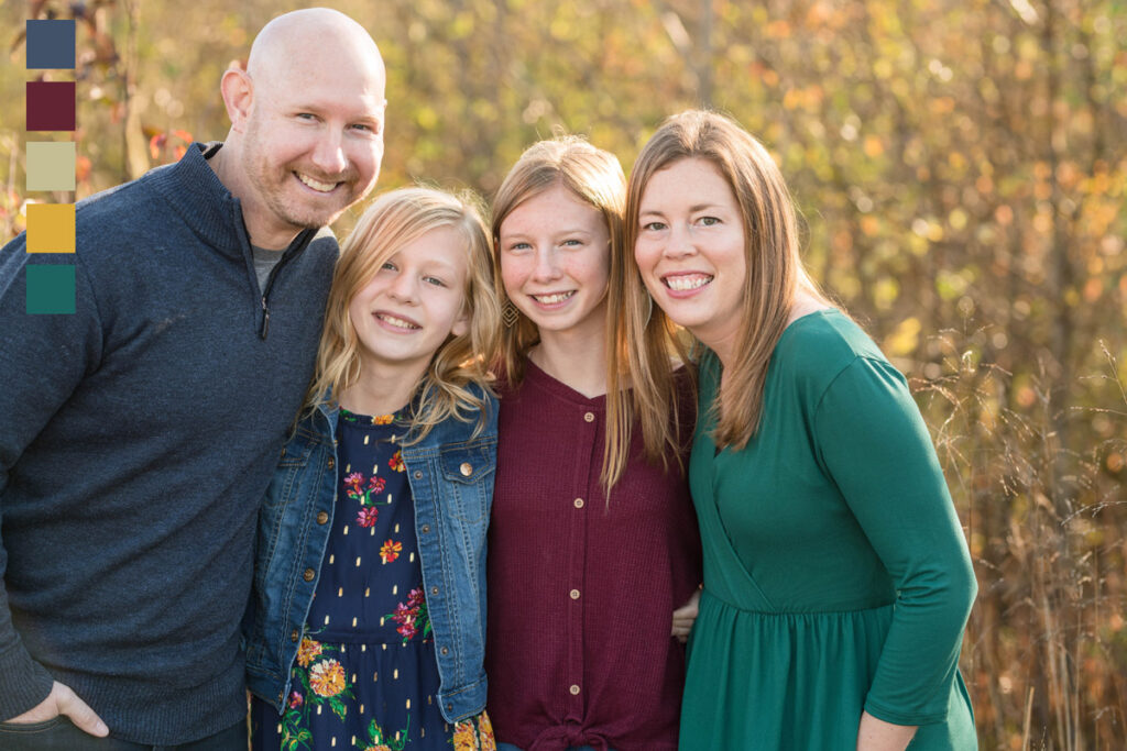 Family of four smiles standing in a meadow.