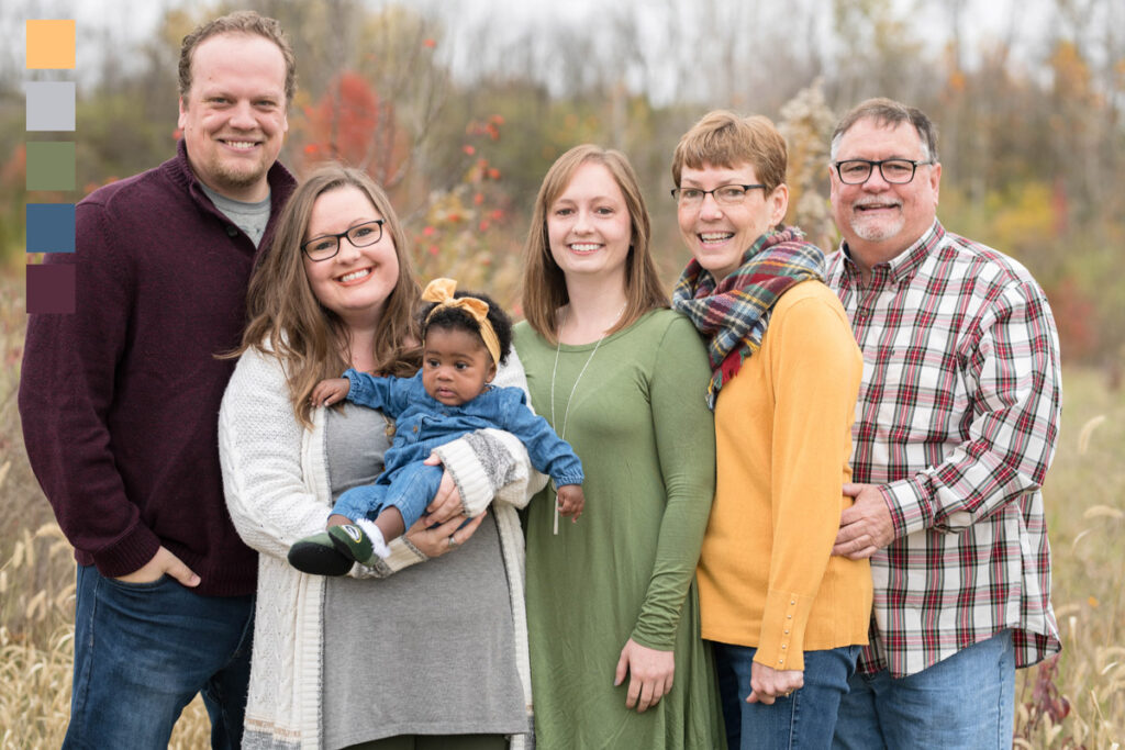 Family of six smiles while standing in a meadow.